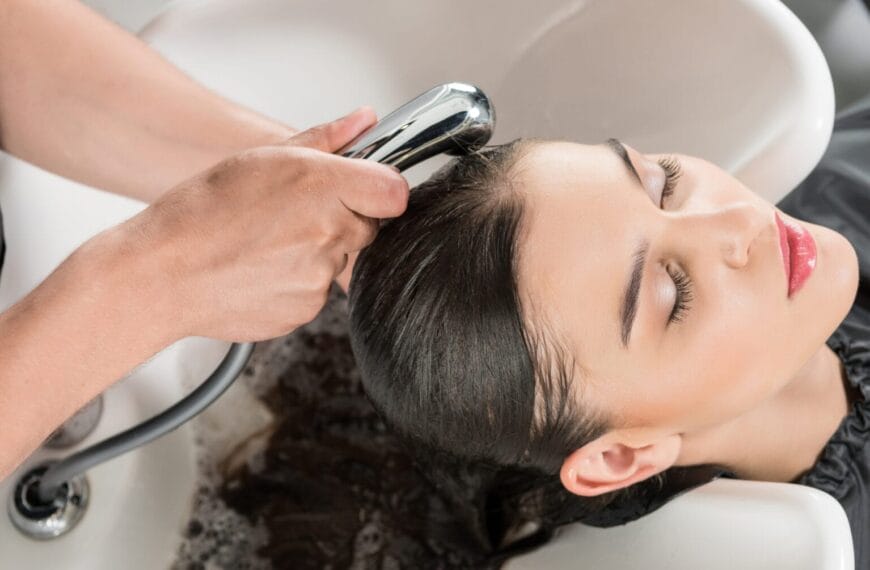 person with eyes closed getting hair washed at a quality grooming salon, water flowing from a hand held nozzle.