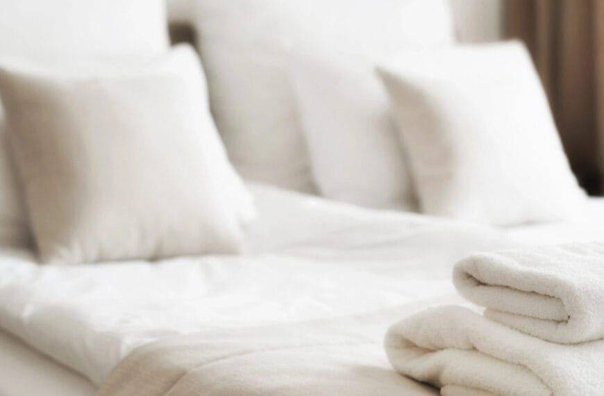 Soft focus of a neatly made bed with white pillows in a bright Iligan hotels room, folded towels included.