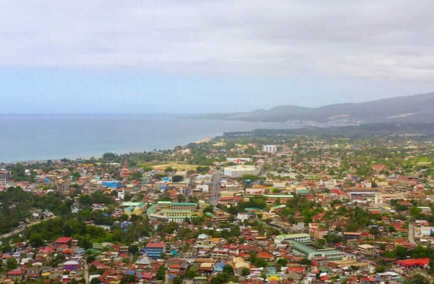 aerial view of a coastal iligan city with colorful rooftops, lush greenery, and hills under a cloudy sky.