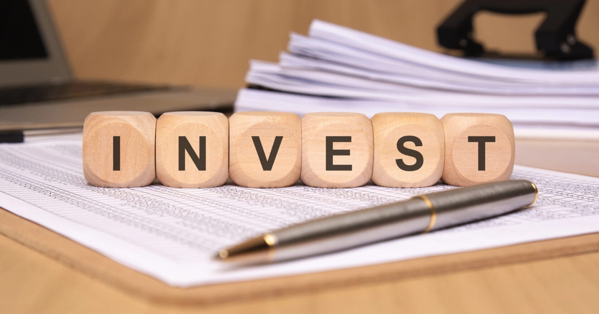 Wooden blocks spelling INVEST ILIGAN on papers with a pen and stacked files in the background.