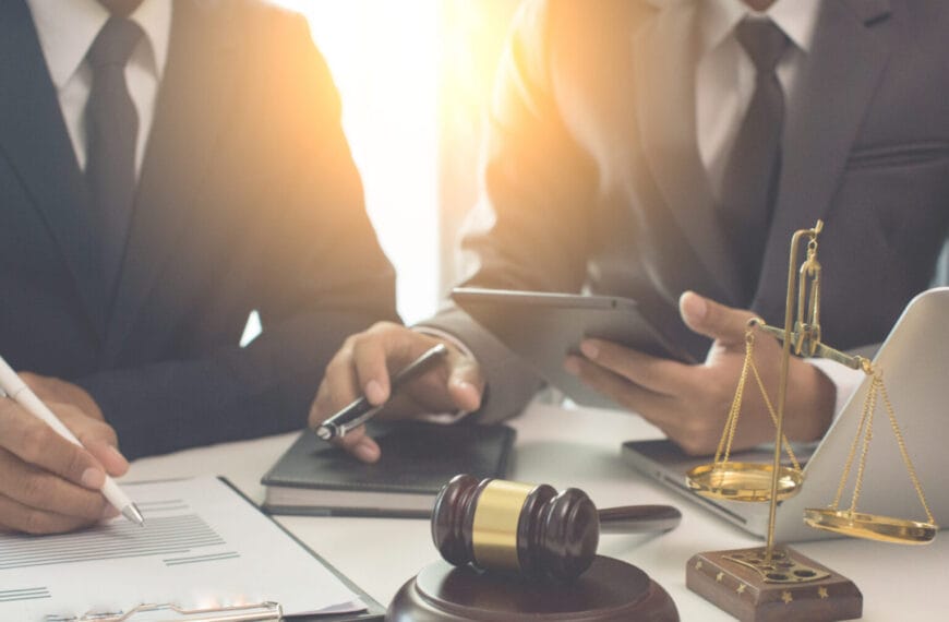 Two people in suits, including an Iligan lawyer, work at a desk with legal documents, a gavel, and a laptop.