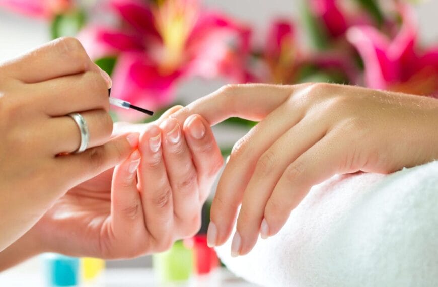 close up of a manicure with a person applying nail polish; pink flowers in the background.