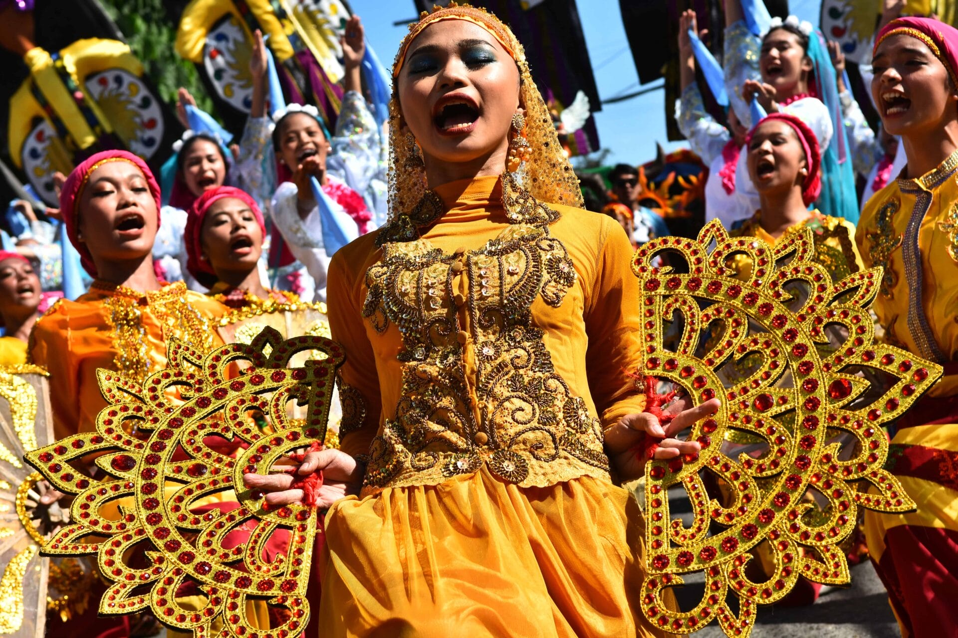 women in ornate yellow costumes dance with decorative fans in a vibrant street parade, perfect for a front page.