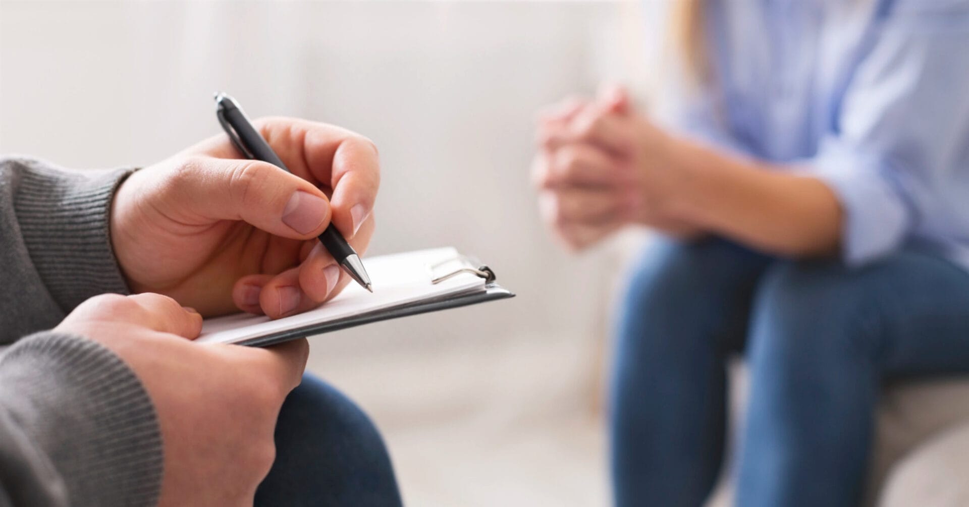 close up of a northern mindanao psychiatrist writing on a clipboard while a person sits across, hands clasped.