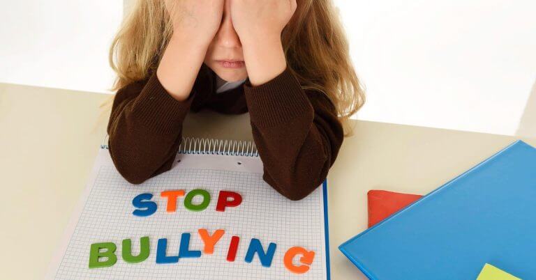 a sad child covers their face at a desk, highlighting iligan city's anti bullying ordinance in colorful letters.