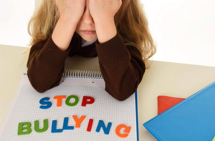 a sad child covers their face at a desk, highlighting iligan city's anti bullying ordinance in colorful letters.
