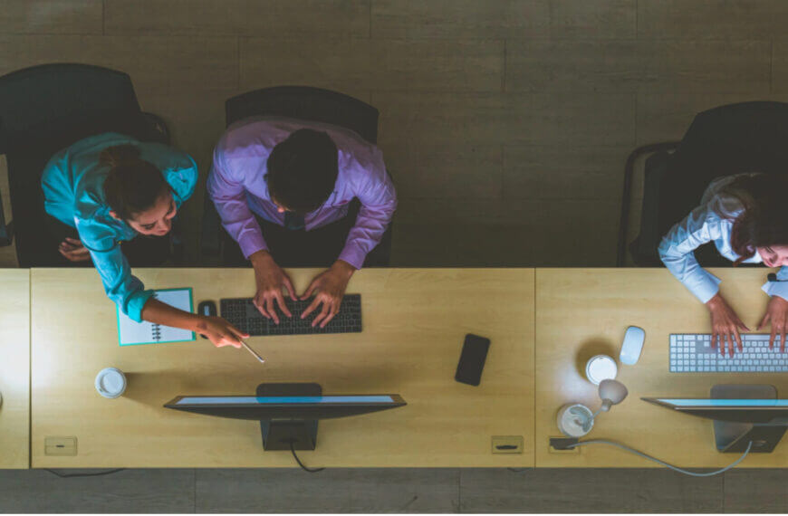 three people work at computers in an iligan city office, two collaborate while one works alone, viewed from above.