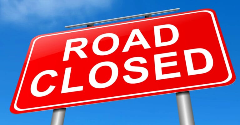 red road closed sign with white text in iligan, mounted on two gray poles under a blue sky.