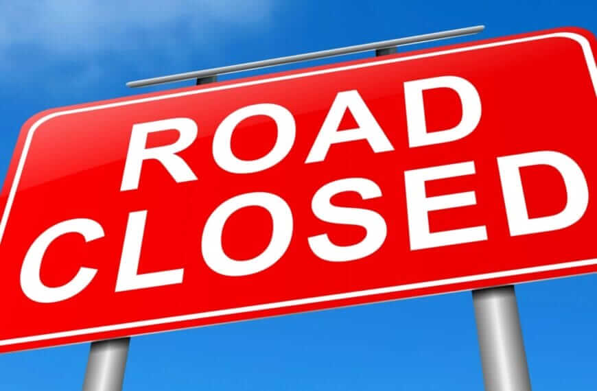 red road closed sign with white text in iligan, mounted on two gray poles under a blue sky.