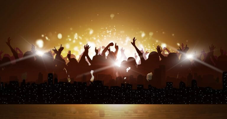 silhouetted crowd with raised hands at a kasadya concert, city skyline below, golden lights shining in the background.