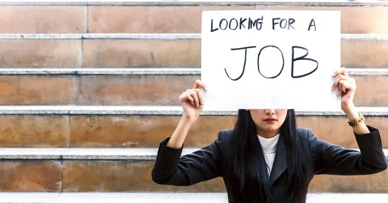 woman in business attire sits on steps holding a sign, "looking for a job," seeking iligan city jobs.