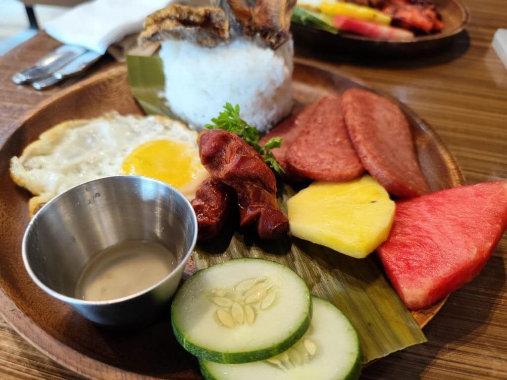 a wooden plate with rice, fried egg, sausage, and more—perfect for any meal at urban coffee studio open 24/7.