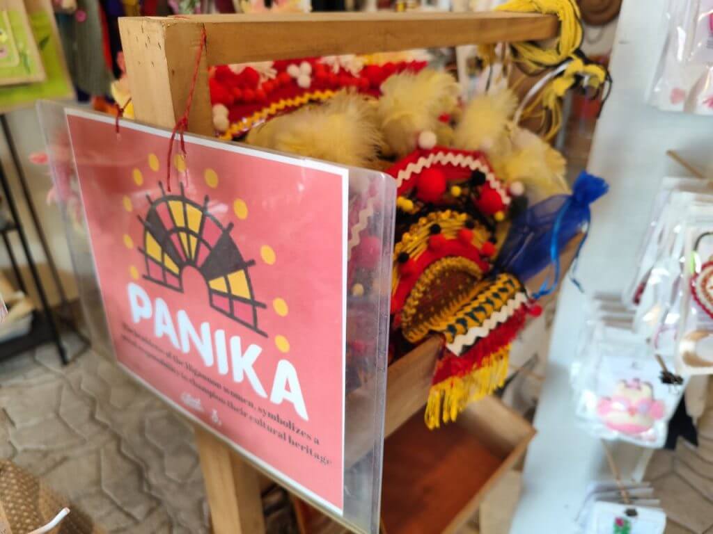 a wooden stand displays traditional headpieces, perfect iligan arts souvenirs, with a red panika sign in front.