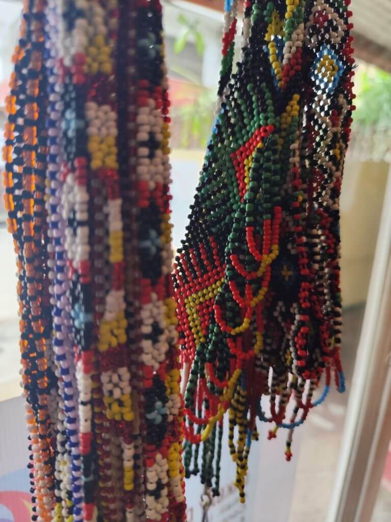 close up of colorful beaded necklaces, showcasing iligan arts and crafts, hanging indoors near a window.