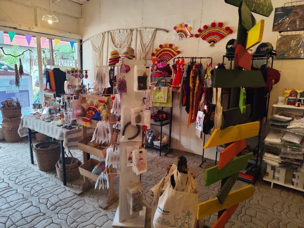 a cozy shop with colorful hats, fans, clothes, iligan arts, and handmade crafts displayed on racks and shelves.