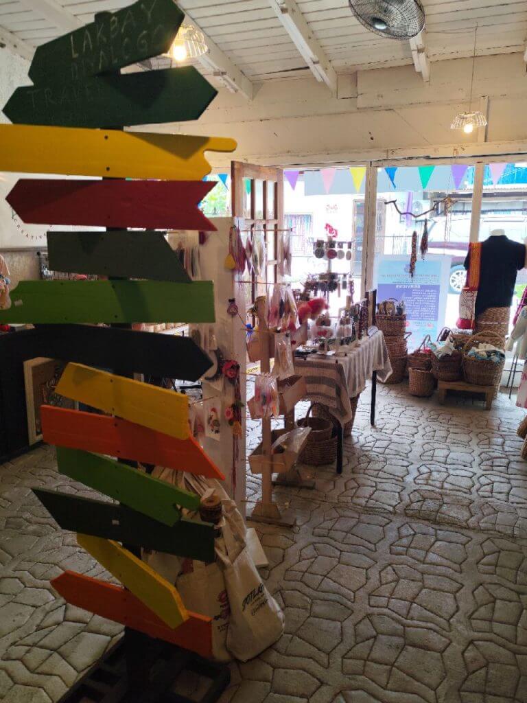 colorful wooden signpost stands inside a cozy shop filled with iligan crafts, baskets, and sunlight through windows.