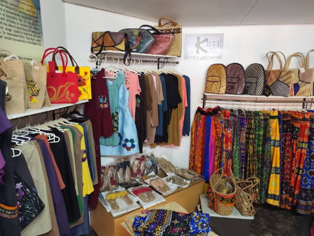 colorful handmade clothing, bags, hats, and sandals&mdash;unique iligan arts and crafts souvenirs on white racks and shelves.