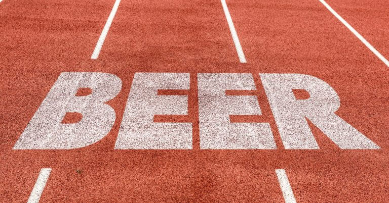 the word beer is painted in large white letters on a red running track between lane lines.
