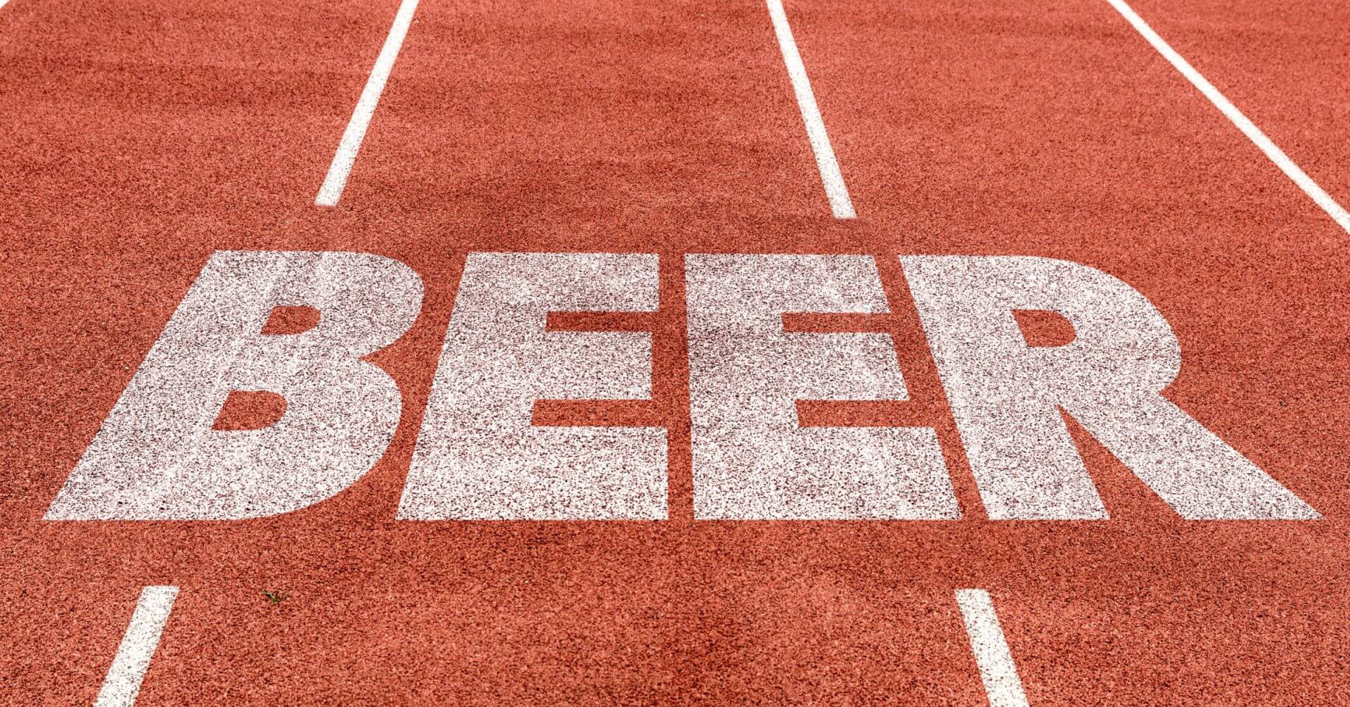 the word beer is painted in large white letters on a red running track between lane lines.