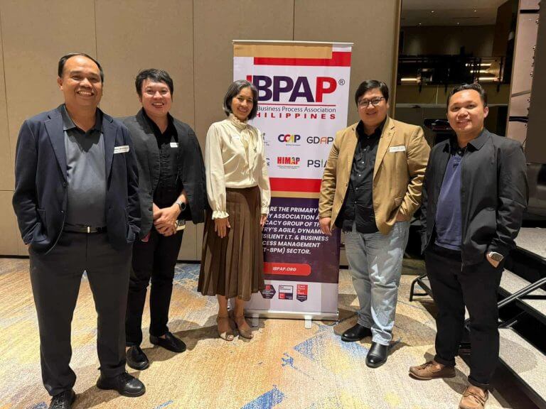 five people in business attire smile beside a bpap banner at an iligan it bpm event.