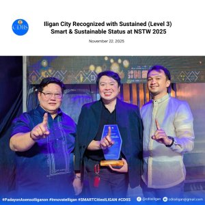 three men smile and hold up one finger; the man in the middle holds a blue and gold award on stage.