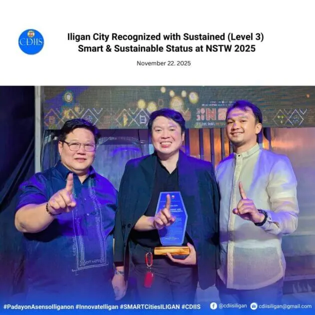 three men smile and hold up one finger; the man in the middle holds a blue and gold award on stage.