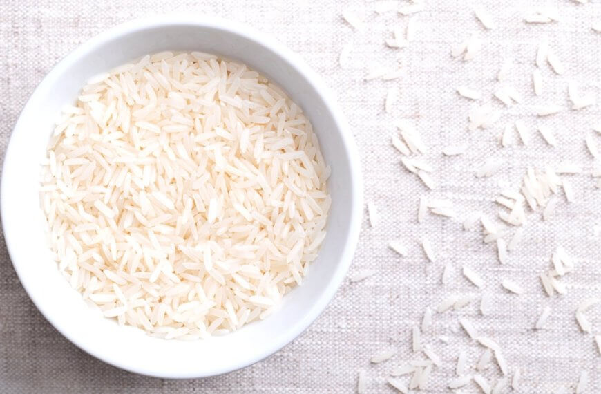white bowl filled with uncooked dinorado mabango rice, grains scattered on a light fabric.
