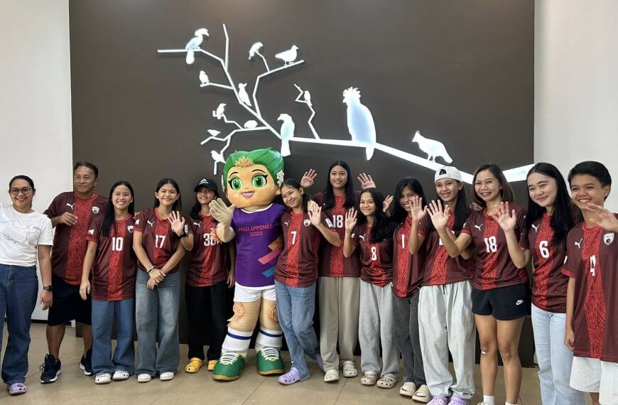a group of people in red sports jerseys and a mascot wave, standing in front of a wall with bird silhouettes.