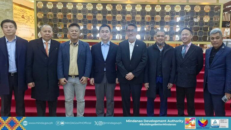eight men in suits stand in a row on red carpeted stairs in front of a decorative wooden wall.