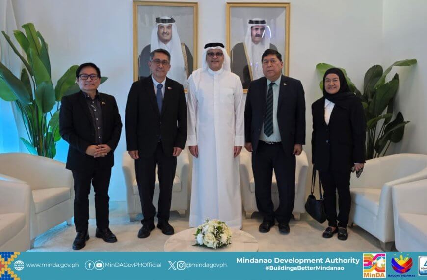 five people in formal attire pose indoors; framed portraits and flags decorate the background.