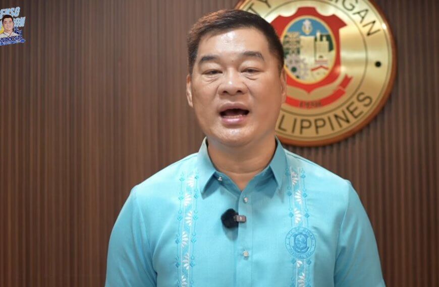 Mayor Siao in a blue barong speaks with the iligan city seal and a sign on measles vaccines behind him.
