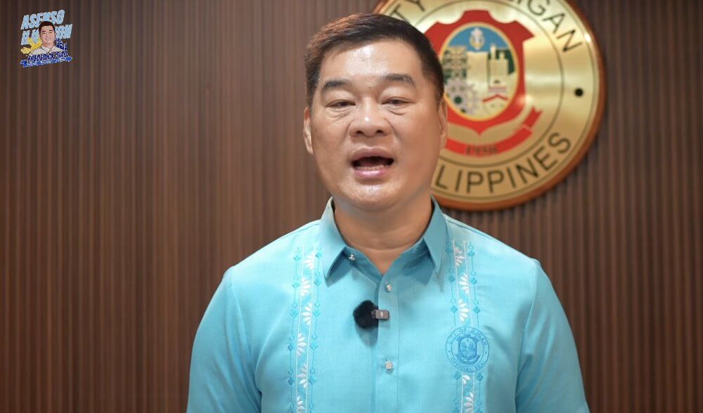 Mayor Siao in a blue barong speaks with the iligan city seal and a sign on measles vaccines behind him.