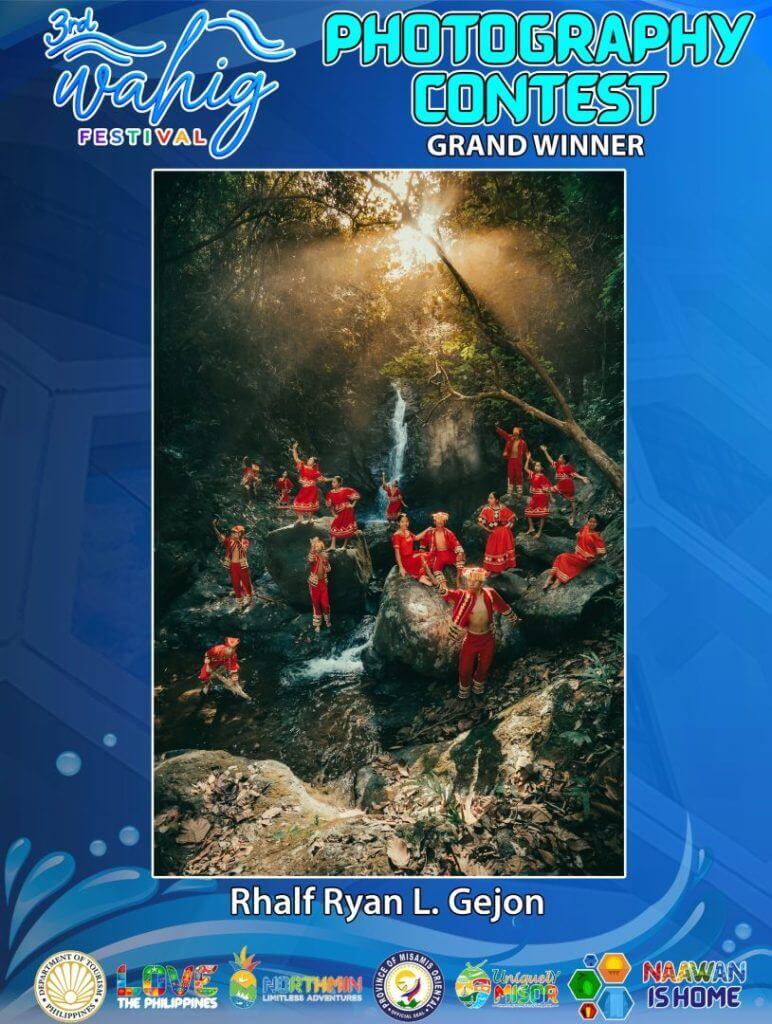 a group in red outfits poses on rocks by a forest waterfall, sunlight streaming through the trees.